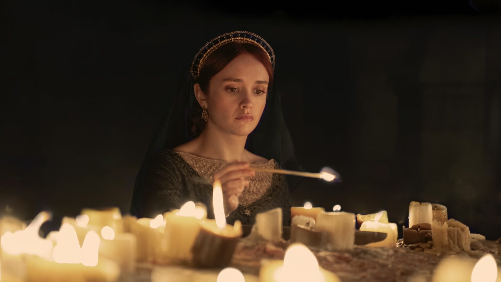 Alicent Hightower lighting candles at an altar, wearing a green dress and black veiled headdress.