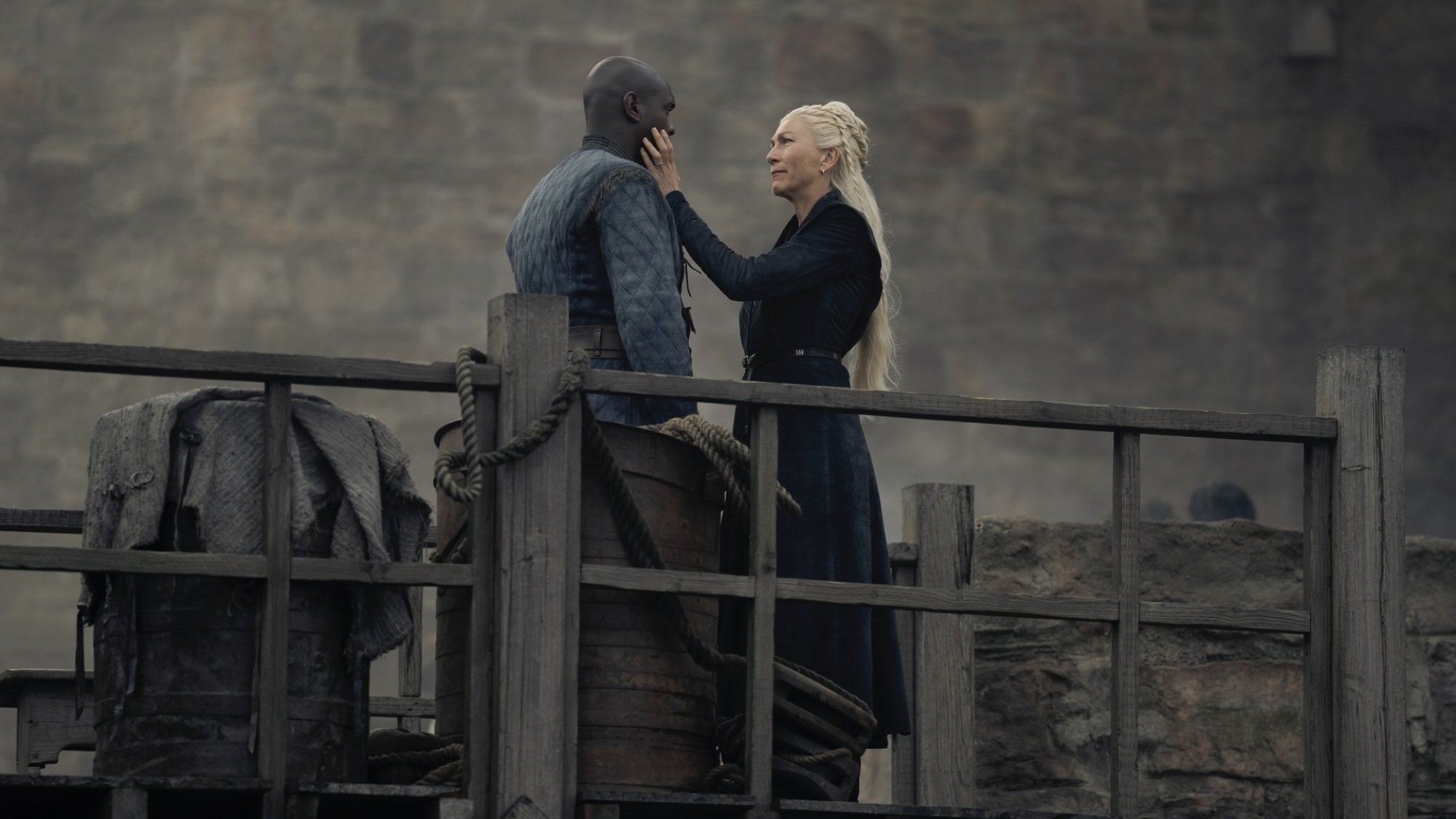 Rhaenys Targaryen cups Alyn of Hull's face; the two stand on wooden scaffolding in a shipyard.