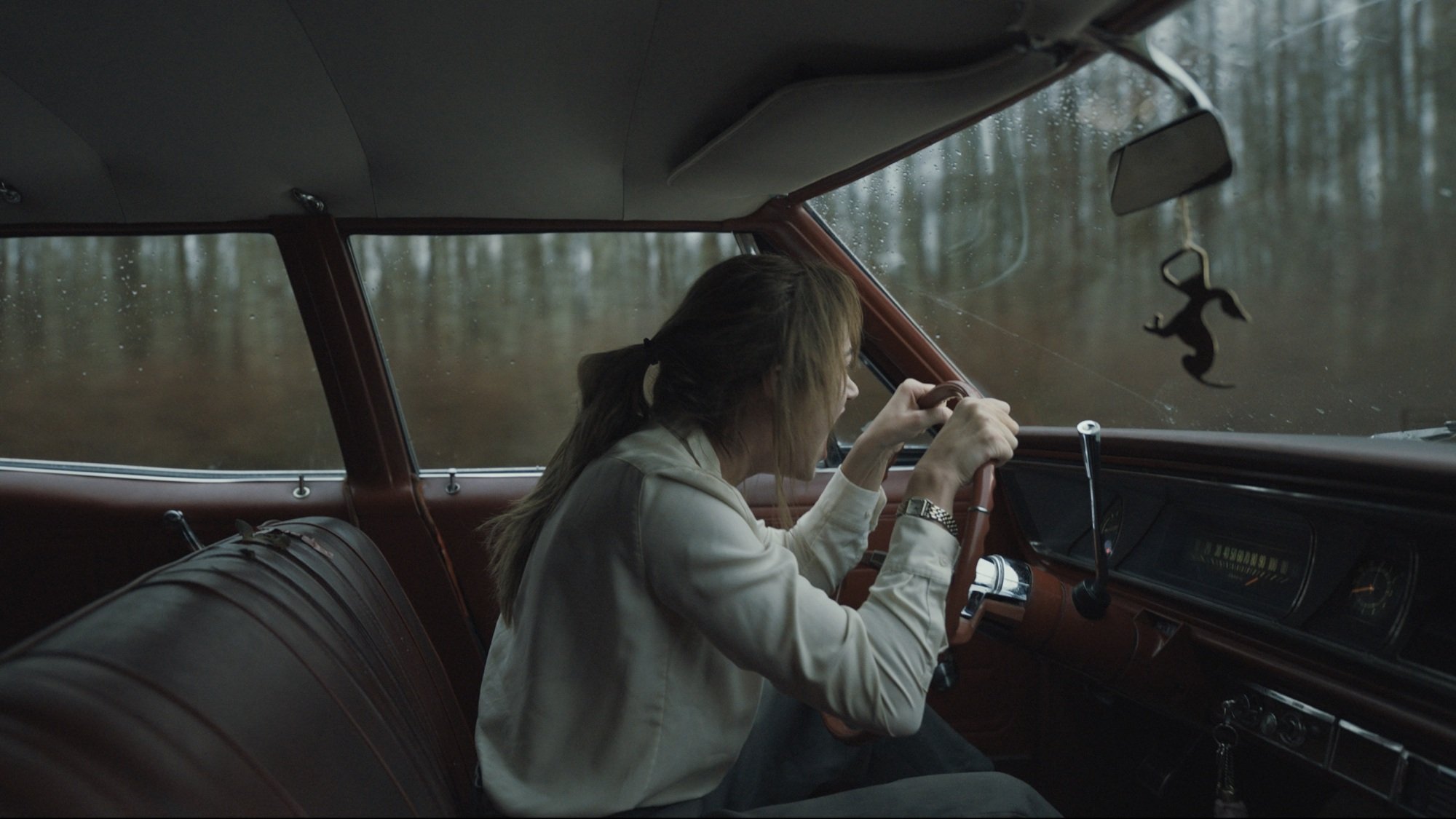 A woman in a white button-up shirt screams while driving her car.