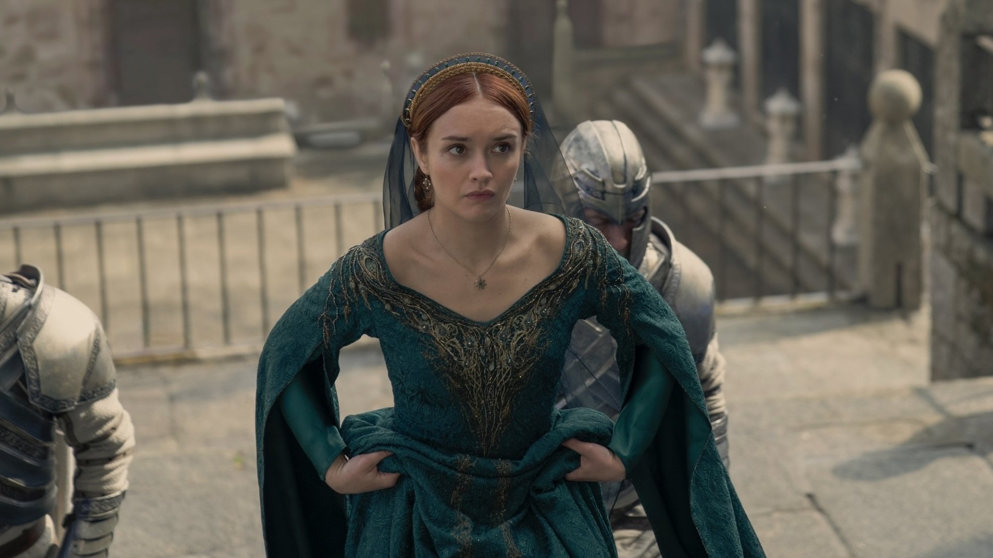 Alicent Hightower walks up the steps leading to the Grand Sept, wearing a green dress and flanked by two knights in armor.