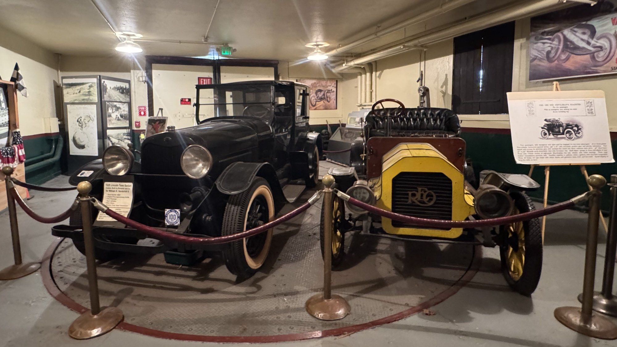 A photograph of two antique cars in a museum, taken on an iPhone 15 Pro Max.