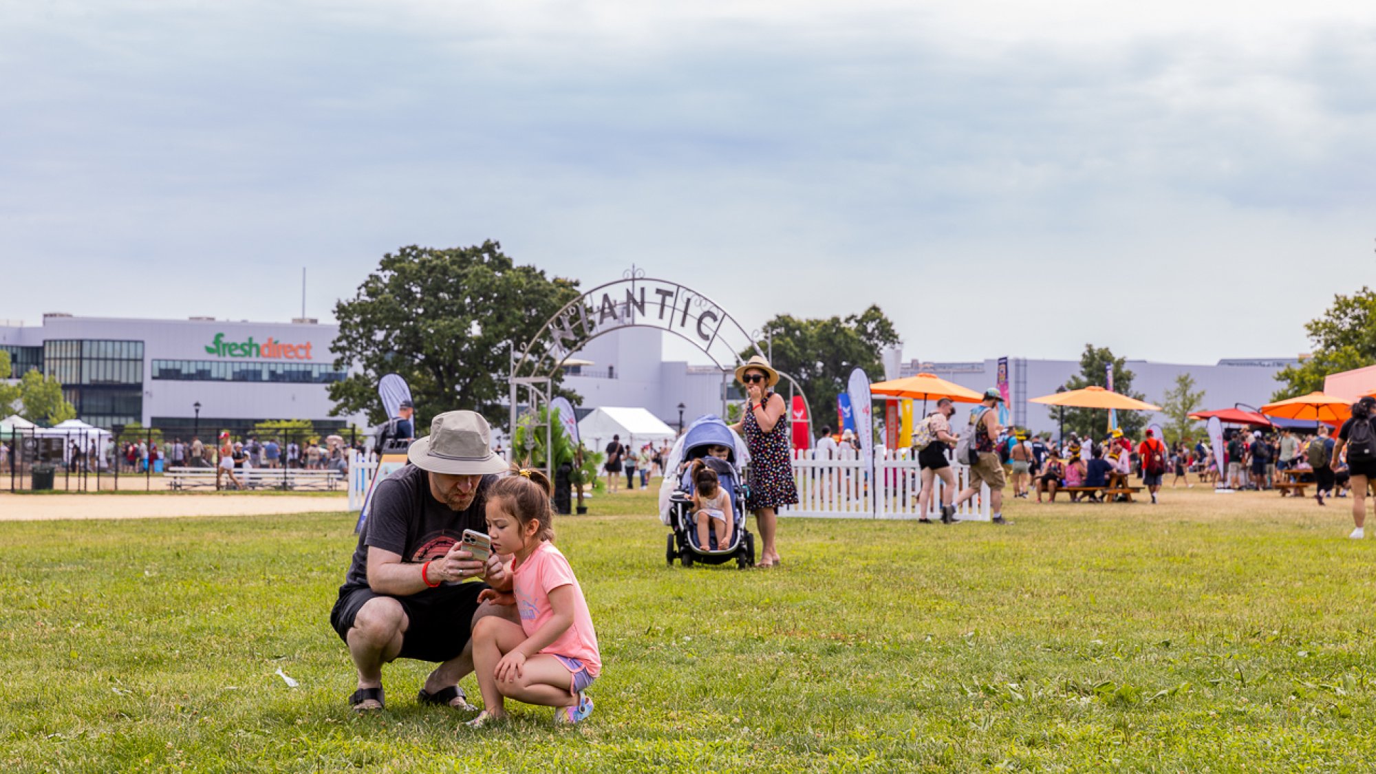 A father and daughter crouch on a lawn, looking at a phone screen together.