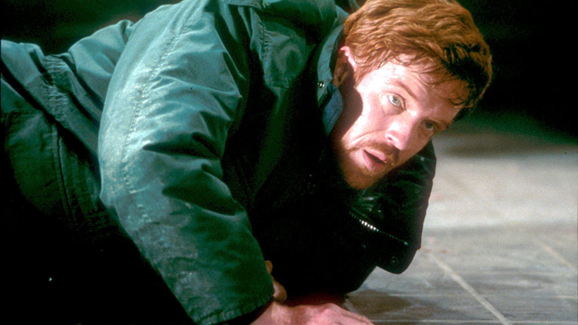 A man in a green jacket looks up from a lying position on the ground.