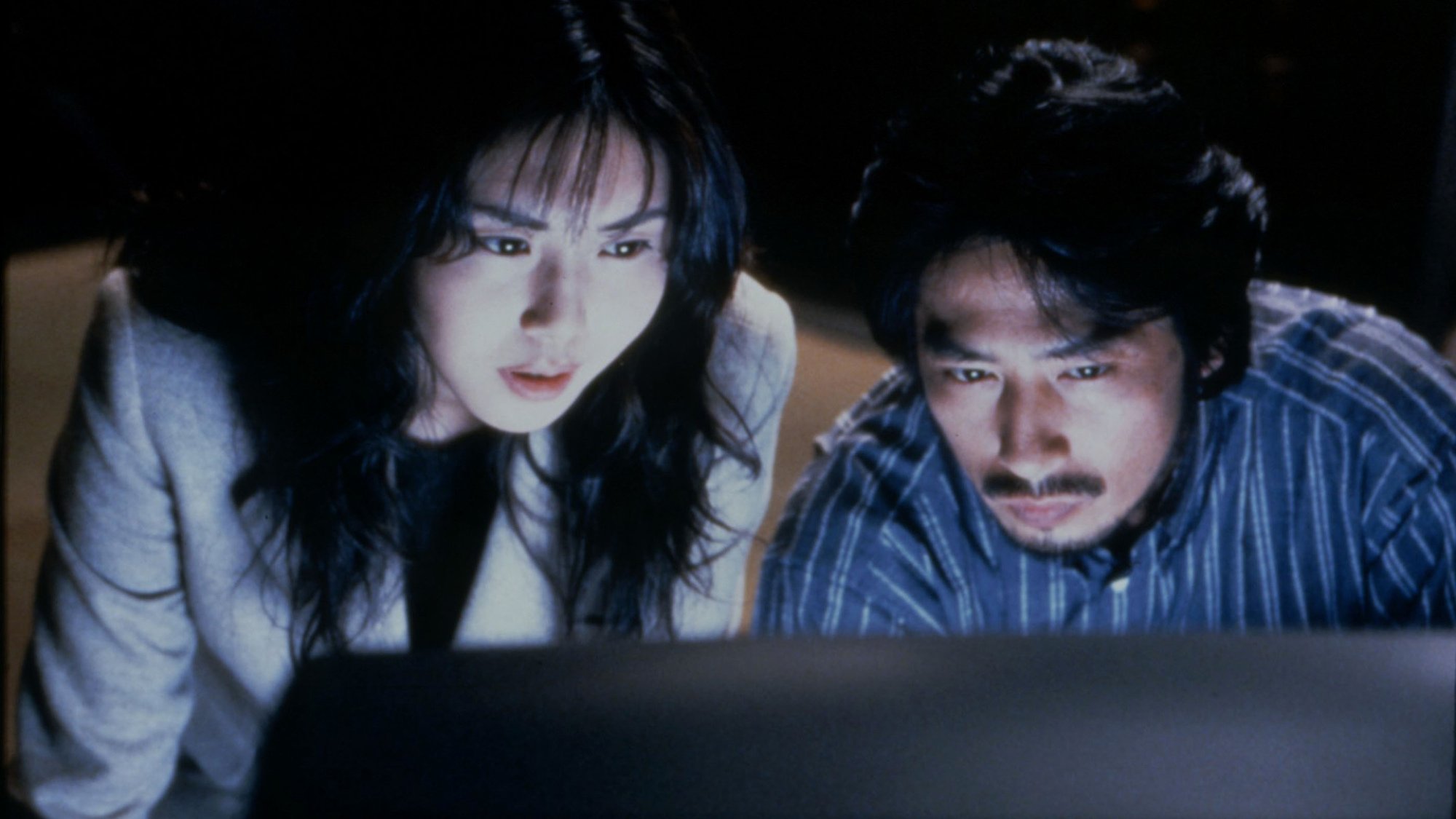 Two people look serious while staring at a television.