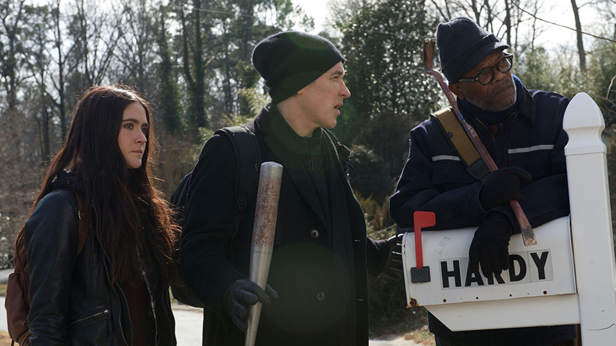 A woman stands next to a man holding a baseball bat, next to a man leaning on a letterbox reading "Hardy."