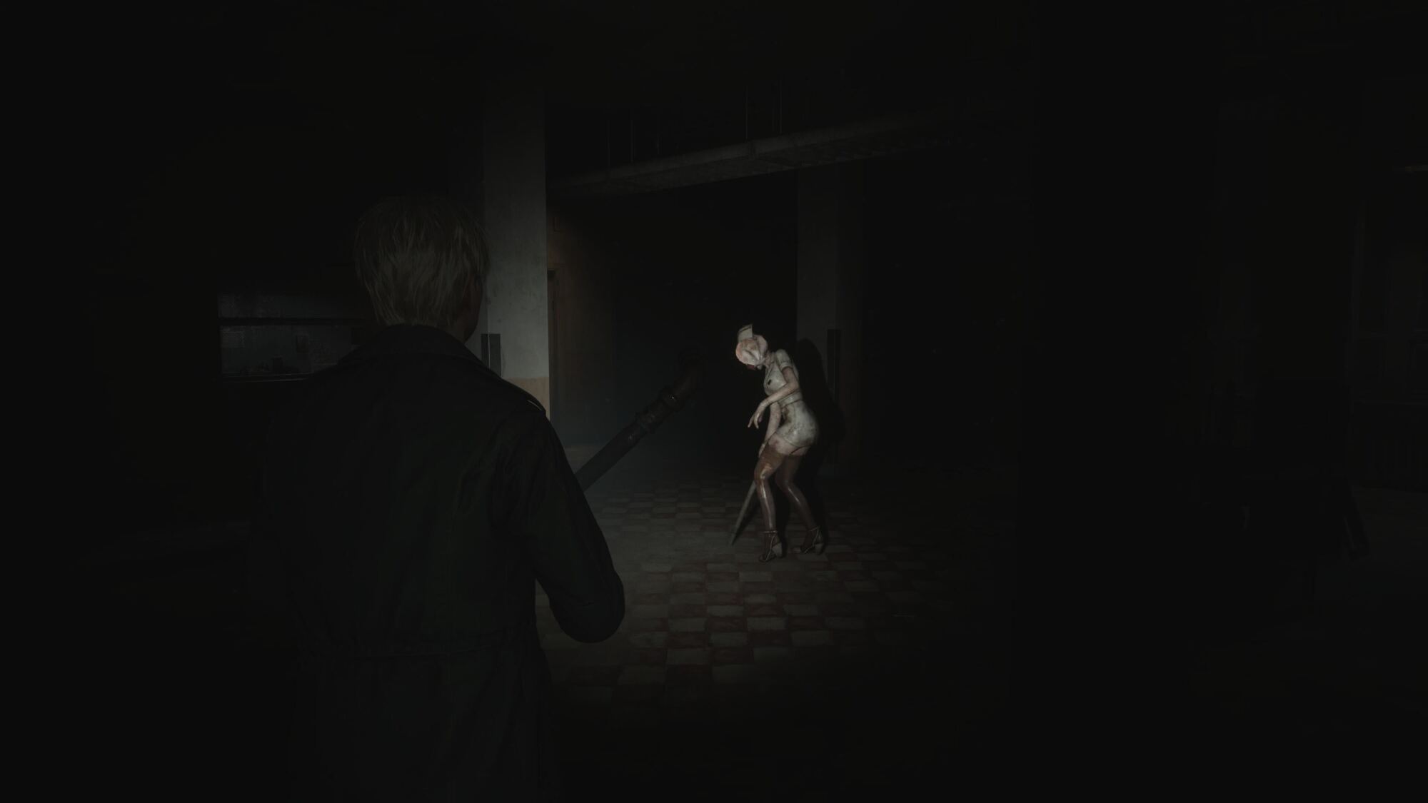 In a dark and dimly lit room, a man stands holding a weapon as he faces two twisted, humanoid creatures. The creatures have bandaged heads and distorted bodies, resembling nurses in grotesque form, standing in a threatening pose, bathed in faint light