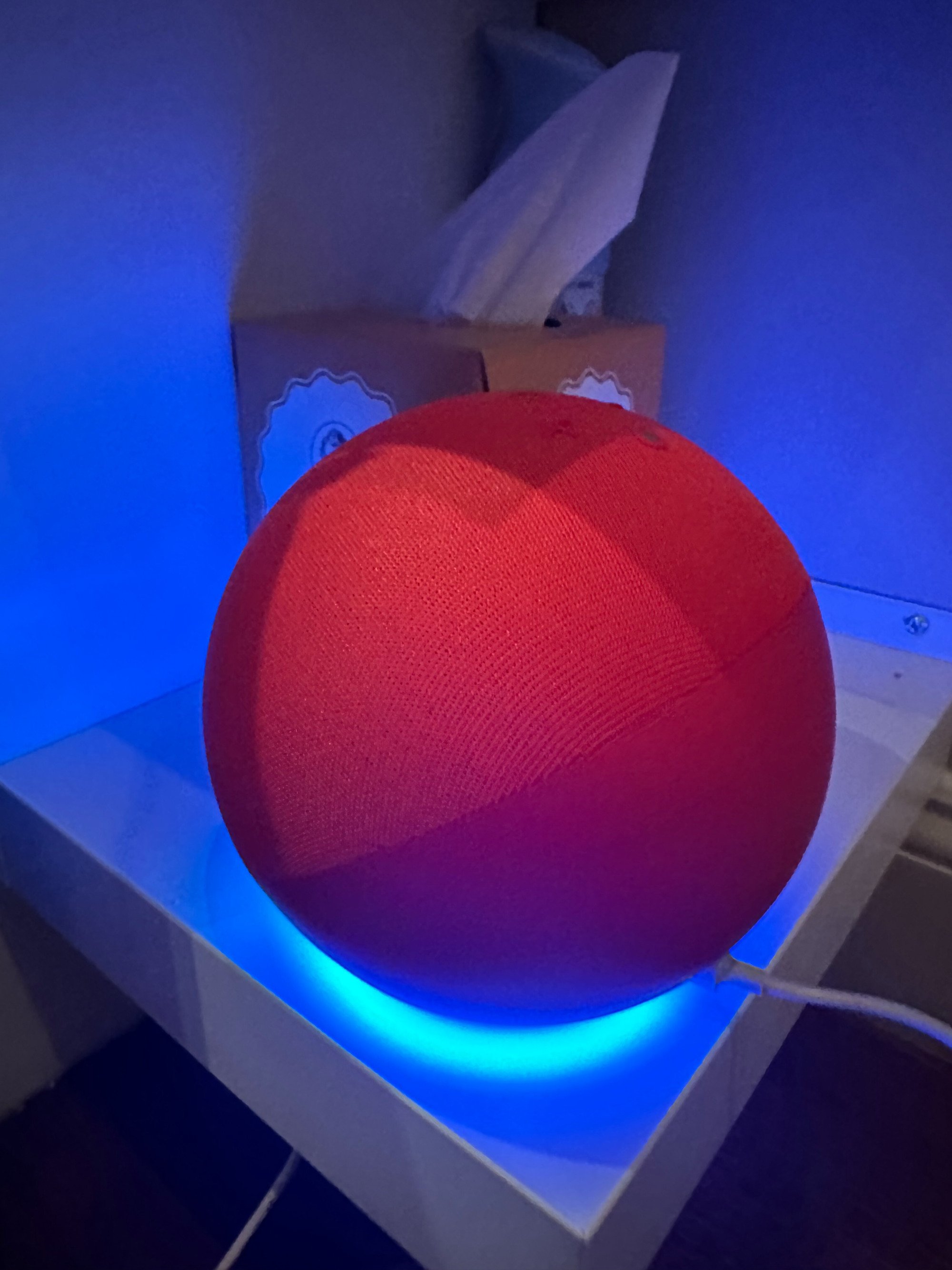 The 4th Gen Amazon Echo glowing with a blue color on the bottom while resting on a shelf