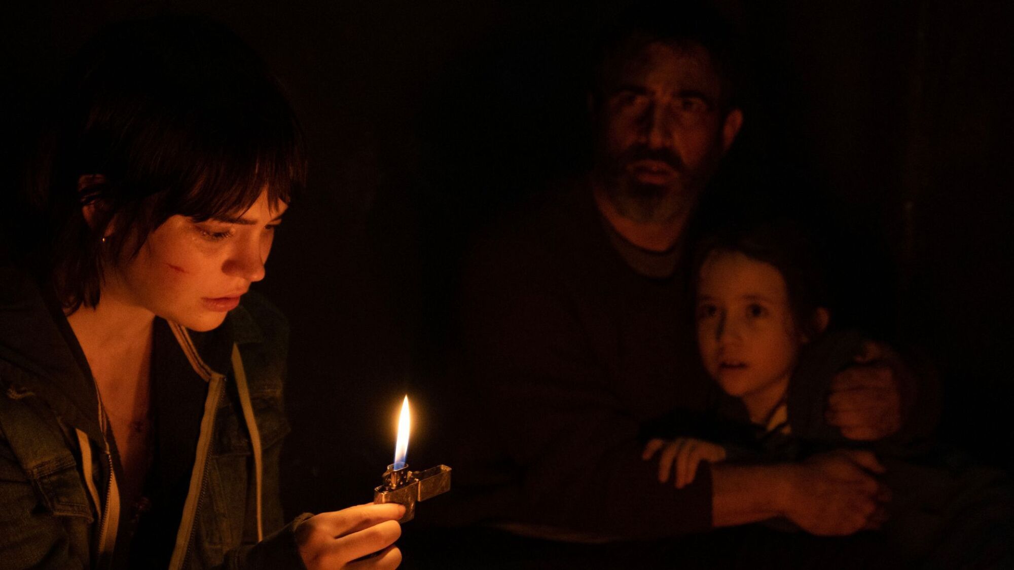 Three people in a pitch black room stare at a lighter flame.