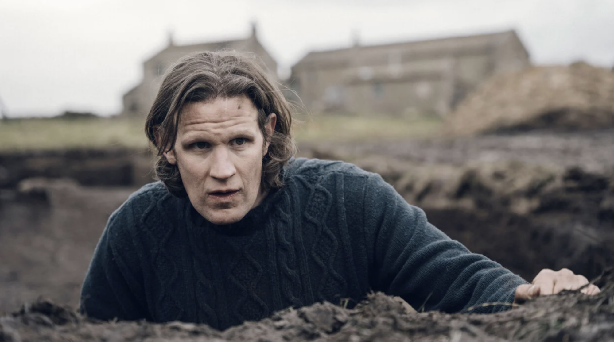 A man stands in a trench in the ground in the countryside.